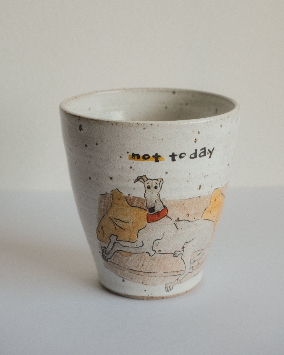 A handmade speckled ceramic cup with a hand-drawn illustration of a dog on a couch and the text 'not today' written on it, set against a plain light background.