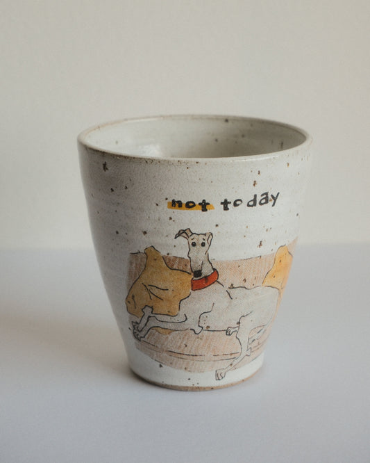 A handmade speckled ceramic cup with a hand-drawn illustration of a dog on a couch and the text 'not today' written on it, set against a plain light background.